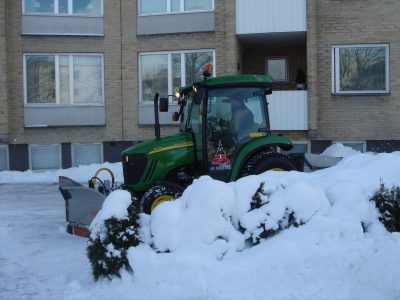 Traktor med snöplog inne på en gård